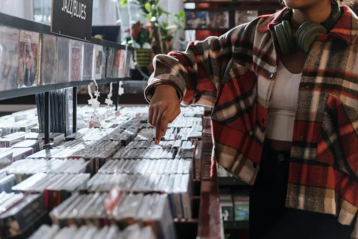 Une personne explore une collection de CD dans un magasin de musique, illustrant la recherche et la sélection minutieuse de sons, une étape clé du métier de designer sonore.