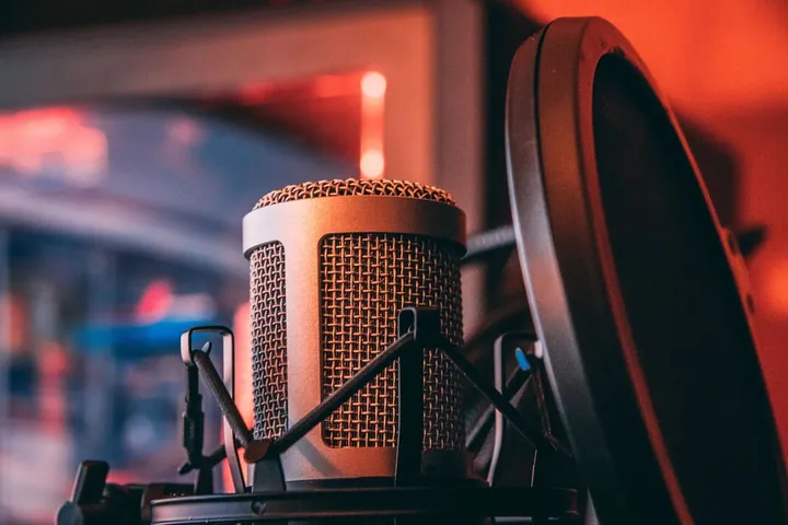 Microphone professionnel de studio ou d'agence sonore avec filtre anti-pop, éclairé par une lumière ambiante rouge, prêt pour l'enregistrement.